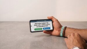 Un teléfono móvil en la mano sobre una mesa, con luz cálida en el que pone: No estás solo Si necesitas hablar llama o envía un mensaje al  024